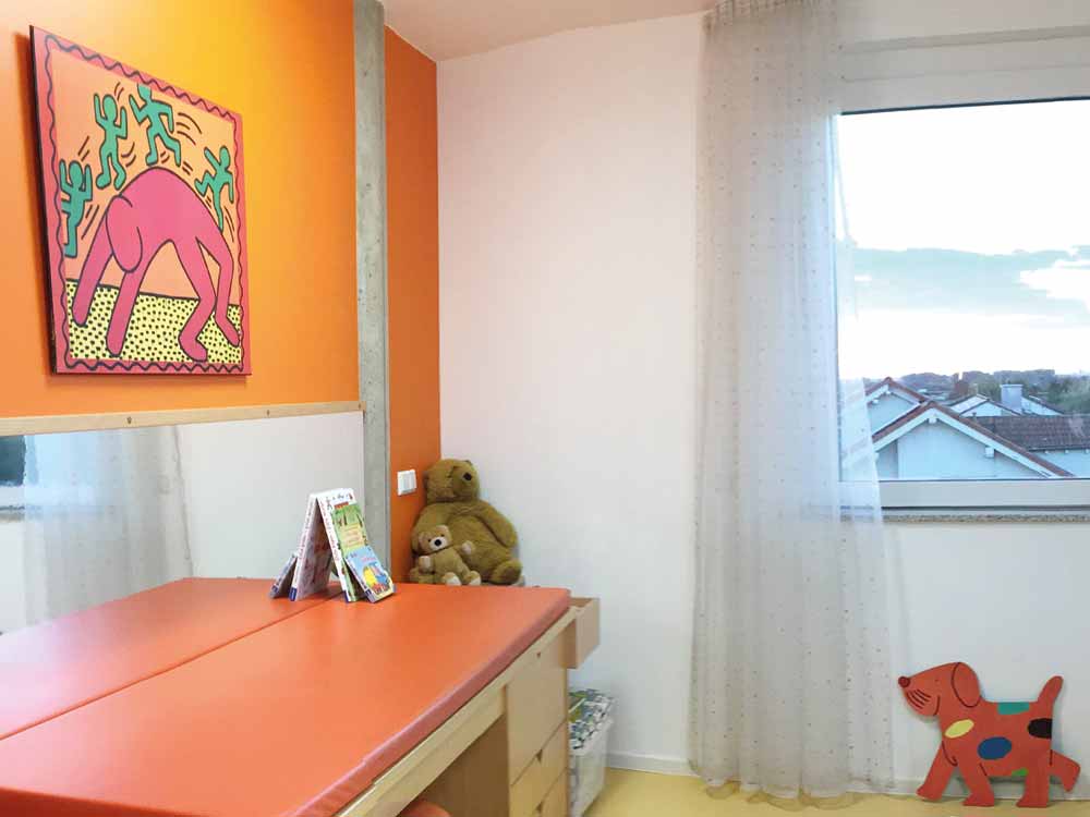 kindgerechtes Untersuchungszimmer mit Bild an der Wand und warmen orangen Farbtönen